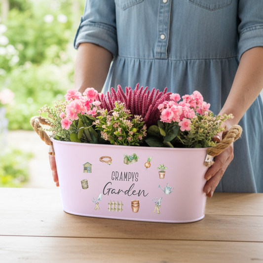 Person holding a pink planter with flowers and 'Grampy's Garden' text