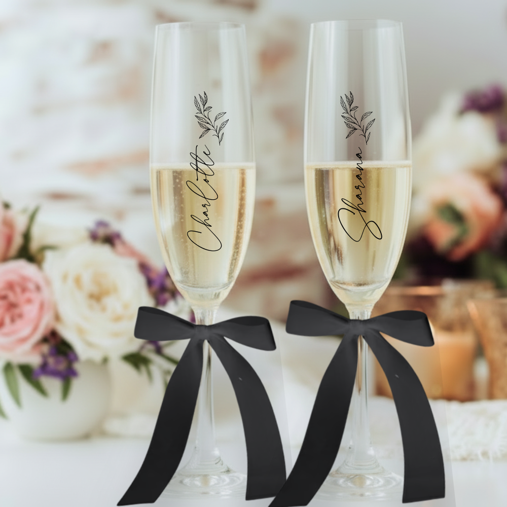 Two champagne flutes with black ribbons and personalized names against a floral background