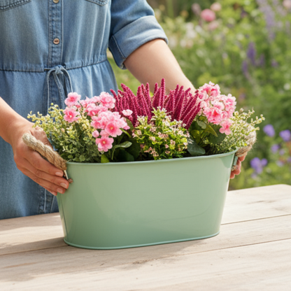Person holding a green metal planter with flowers outdoors