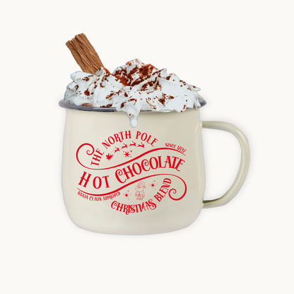Beige mug with red text 'The North Pole Hot Chocolate Christmas Blend' filled with hot chocolate, whipped cream, and a cinnamon stick on a white background.