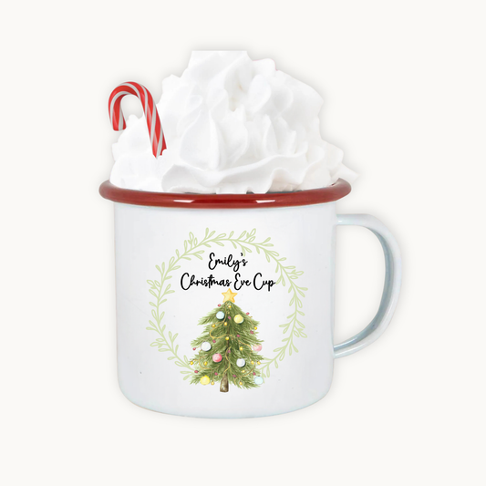 White mug with Christmas tree design and red rim, containing a gift wrapped in white paper.