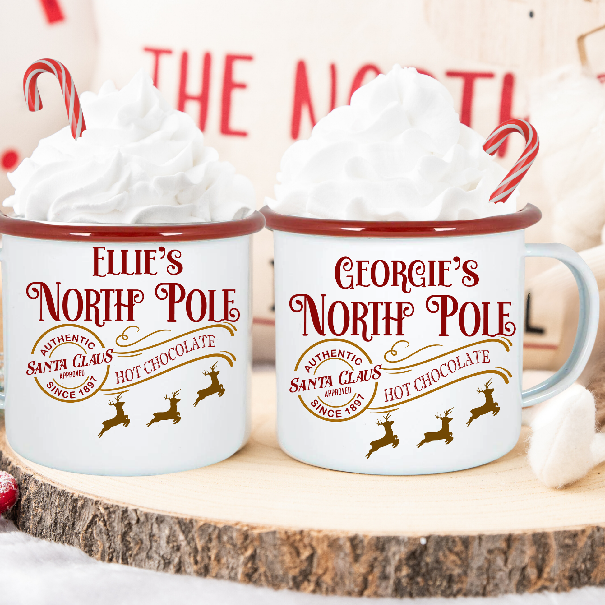 Two mugs labeled 'Ellie's North Pole' and 'Georgie's North Pole' with hot chocolate and whipped cream.