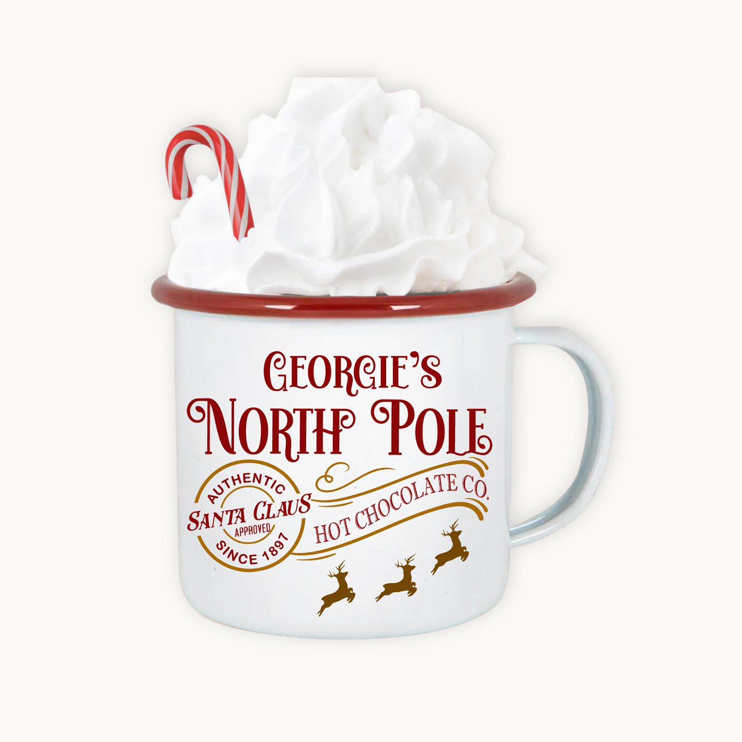 White mug with red rim and 'Georgie's North Pole' text, filled with hot chocolate and whipped cream.