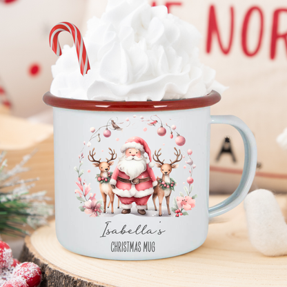 Christmas mug with Santa and reindeer design, filled with hot chocolate and whipped cream, on a wooden surface.