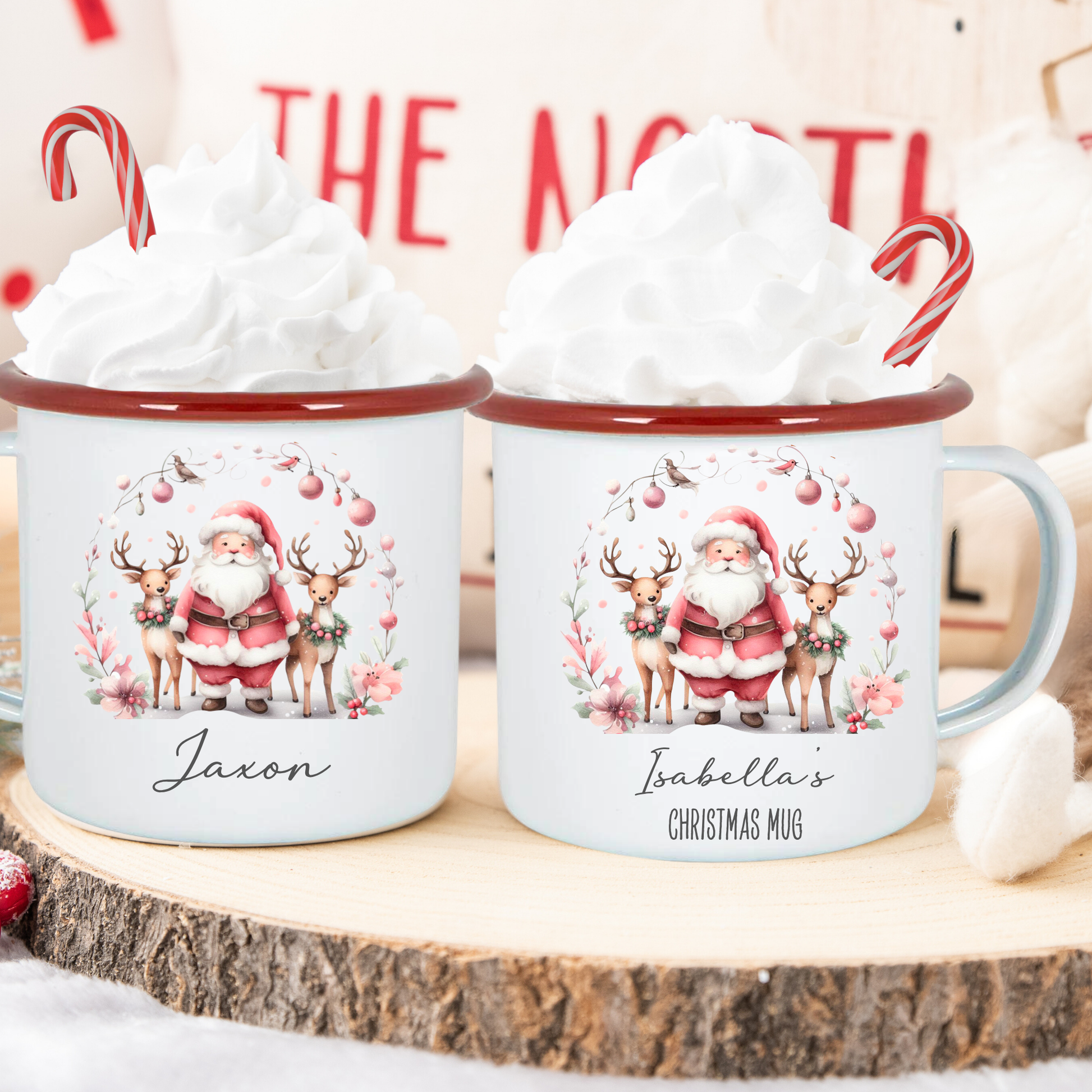 Two Christmas-themed mugs with Santa Claus and reindeer design on a wooden surface.