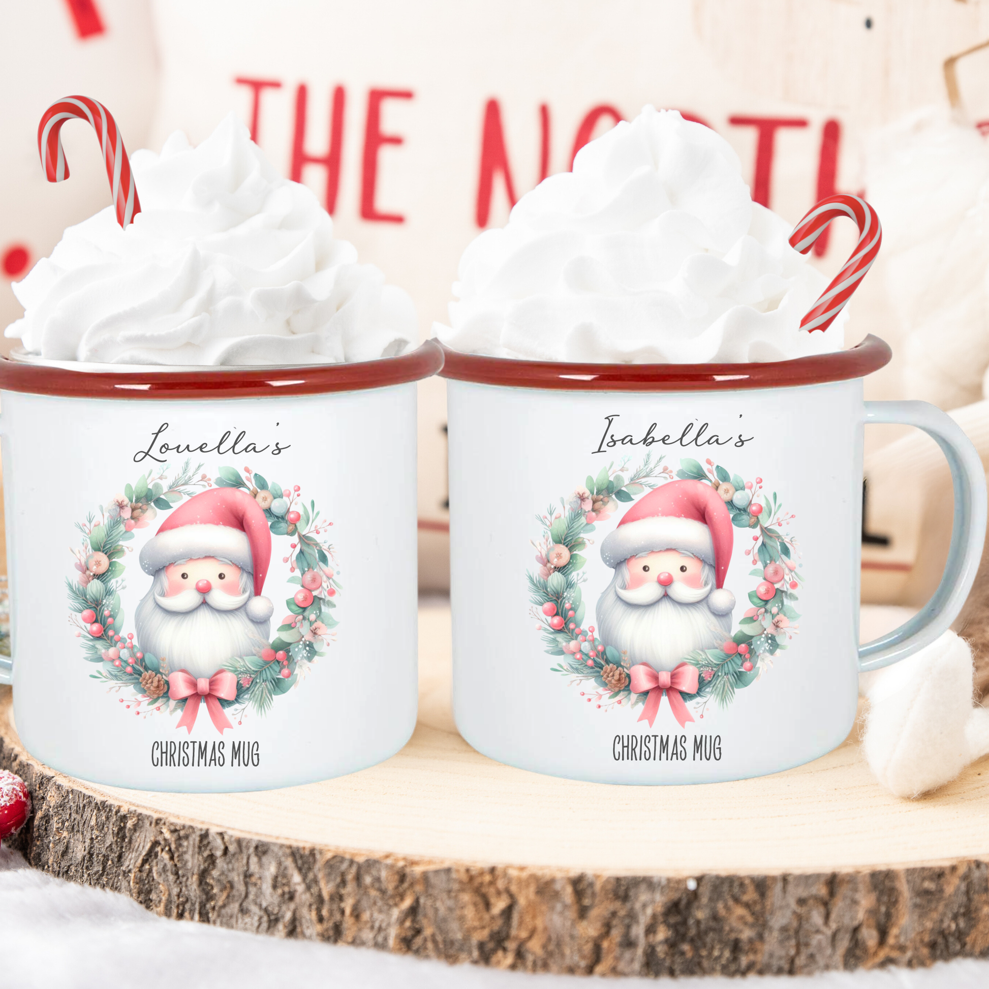 Two Christmas mugs with Santa Claus design on a wooden surface with whipped cream and candy canes.