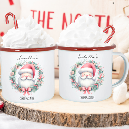 Two Christmas mugs with Santa Claus design on a wooden surface with whipped cream and candy canes.