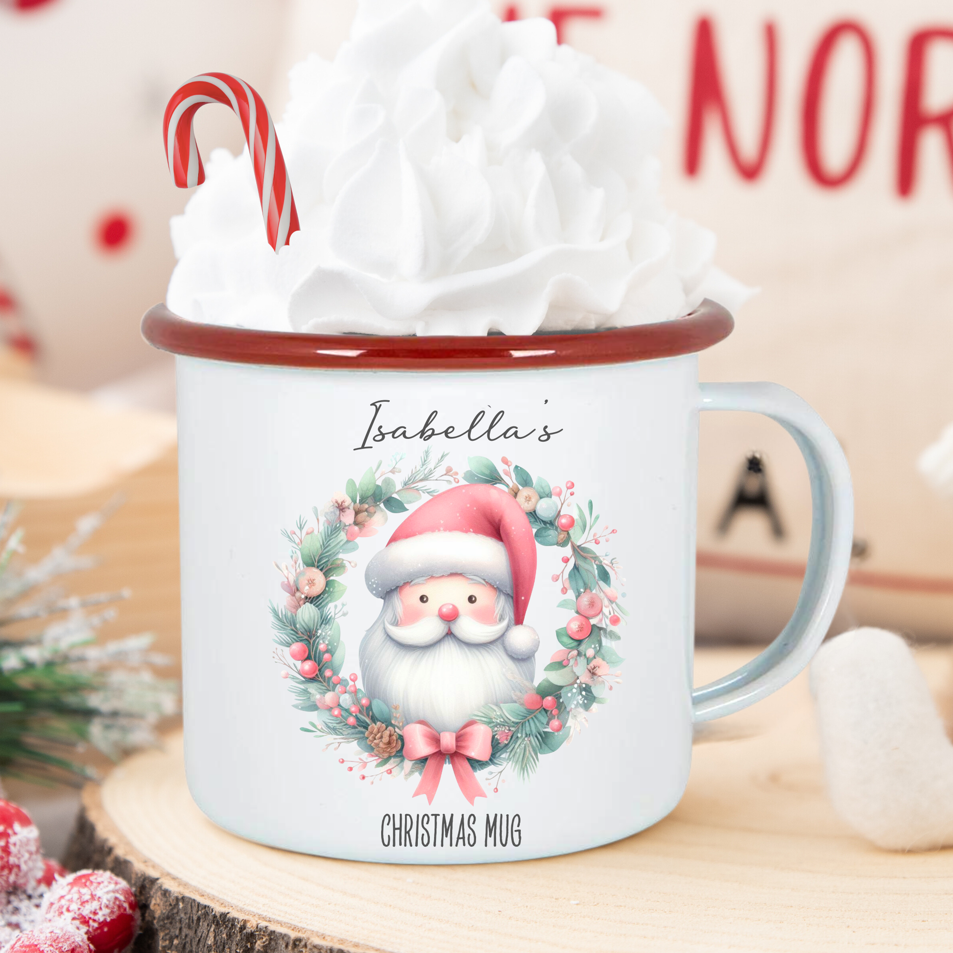 Christmas mug with Santa design, candy cane, and whipped cream on a wooden surface.