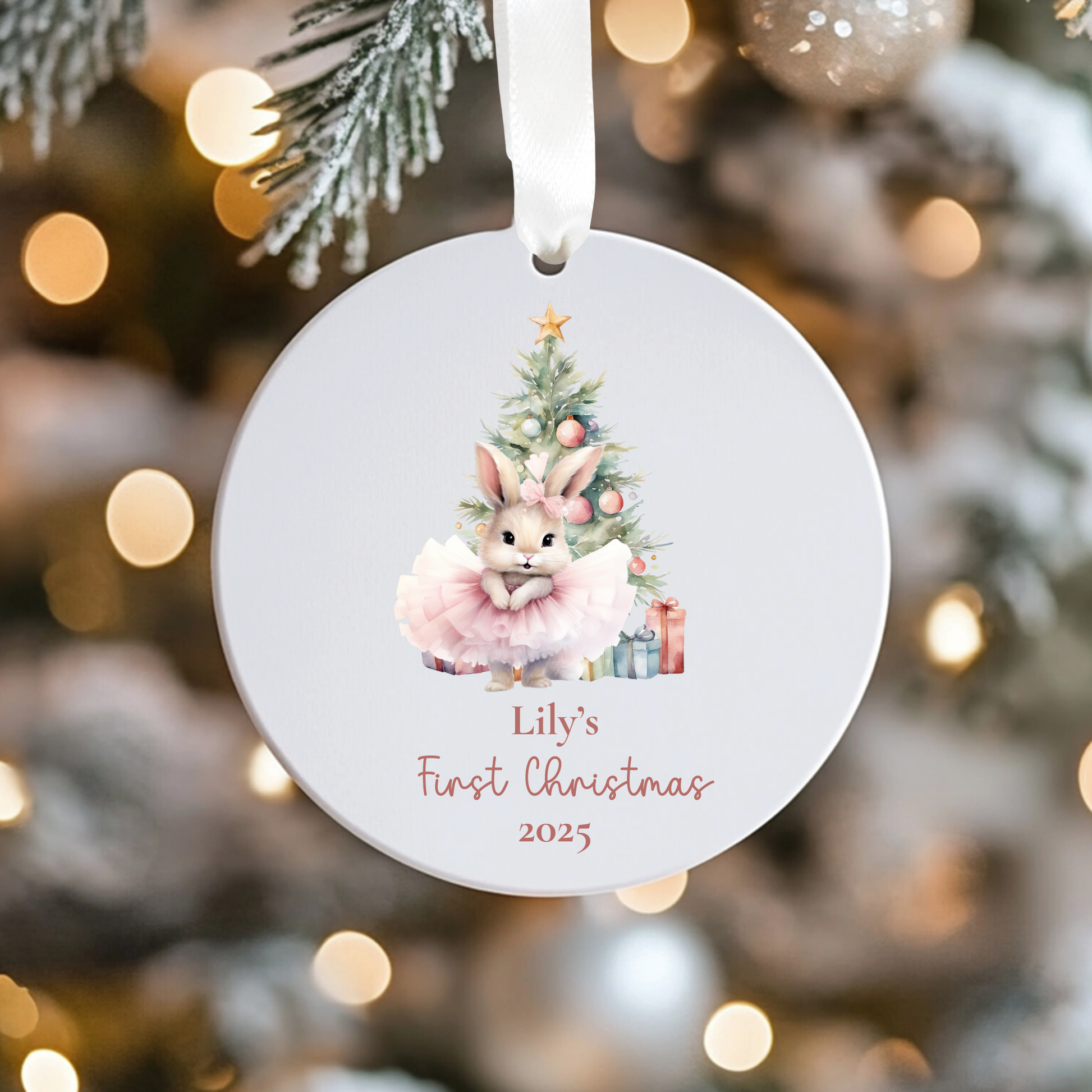 Round Christmas ornament with a rabbit and tree design, personalized for 'Lily's First Christmas 2025', against a blurred festive background.
