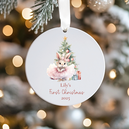 Round Christmas ornament with a rabbit and tree design, personalized for 'Lily's First Christmas 2025', against a blurred festive background.