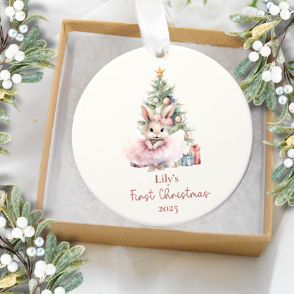 Round Christmas ornament with a bunny and tree design, featuring 'Lily's First Christmas 2023' text, surrounded by festive greenery.