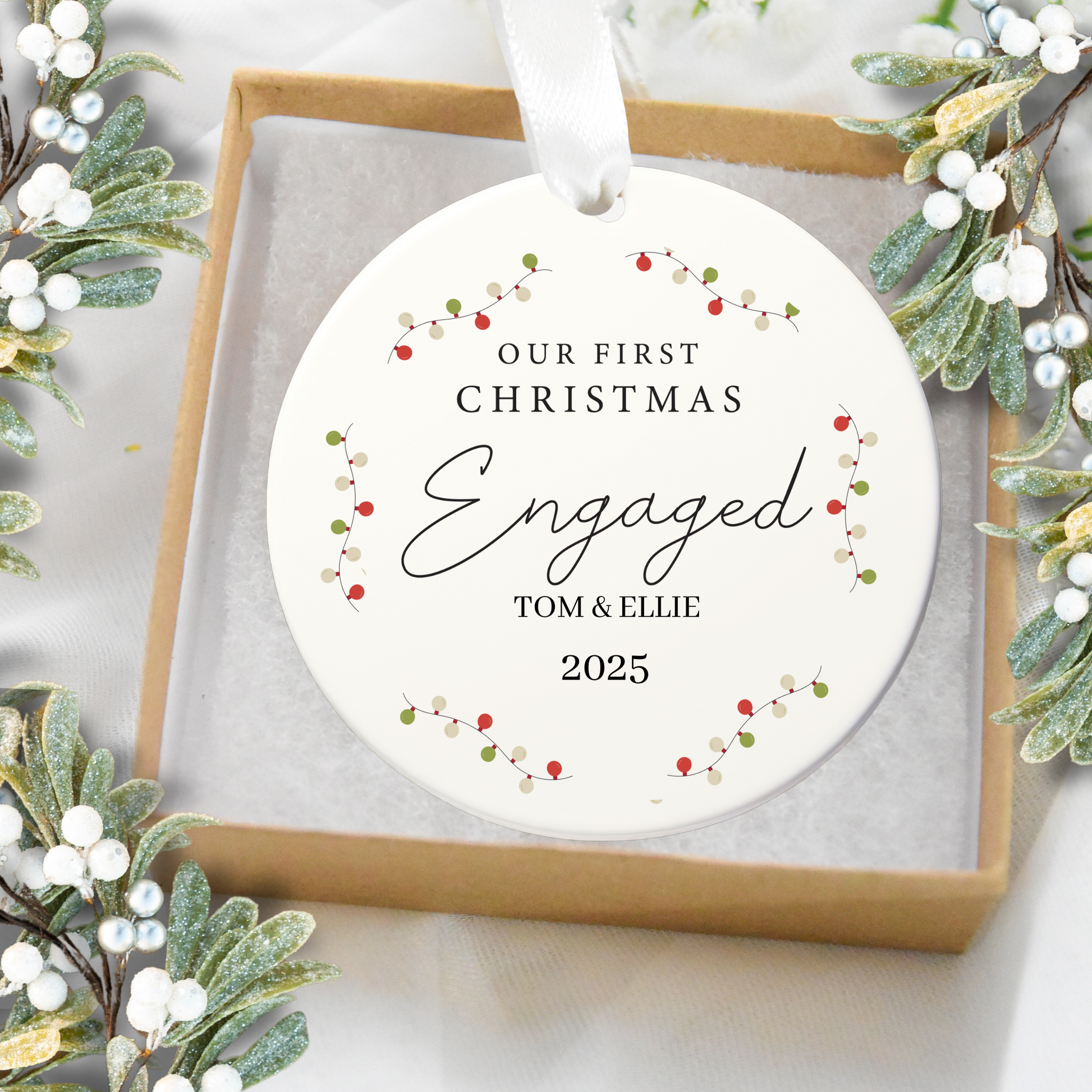 Personalized Christmas ornament with 'Our First Christmas Engaged' text, surrounded by festive greenery.