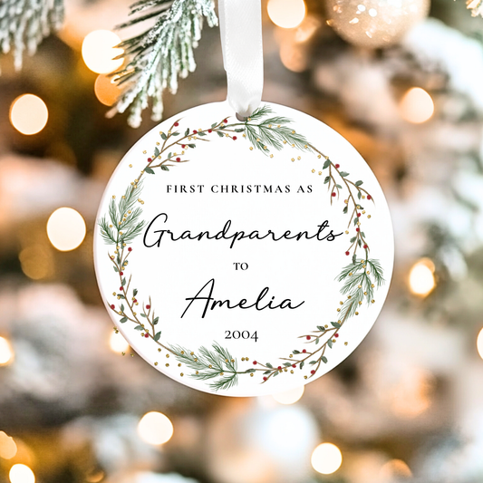 Decorative ornament with text 'First Christmas as Grandparents to Amelia 2004' against a blurred Christmas tree background.