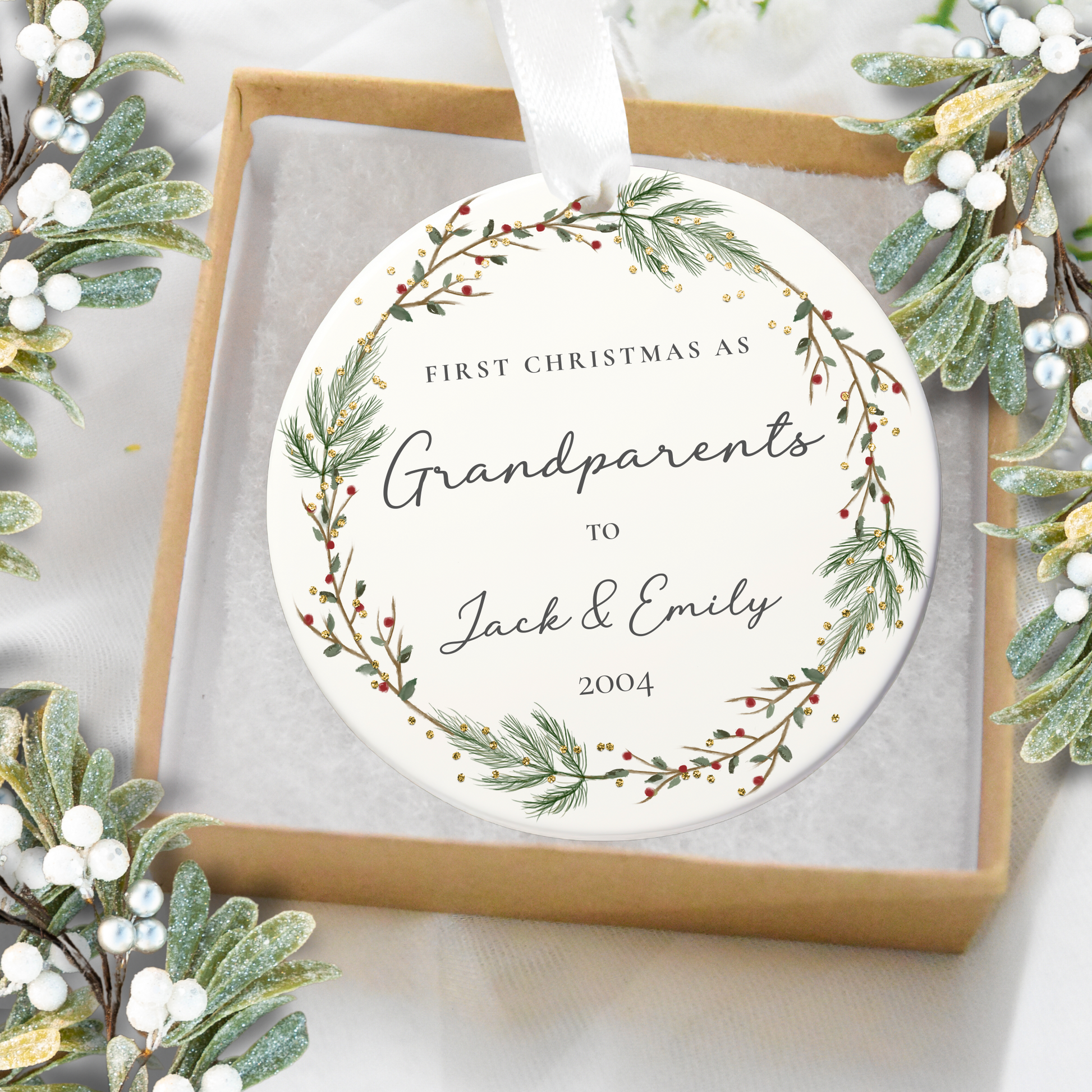 Round ornament with text 'First Christmas as Grandparents to Jack & Emily 2004' surrounded by festive greenery.