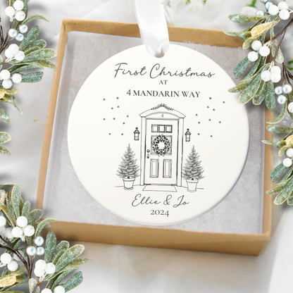 Round Christmas ornament with house illustration and text, surrounded by festive greenery.