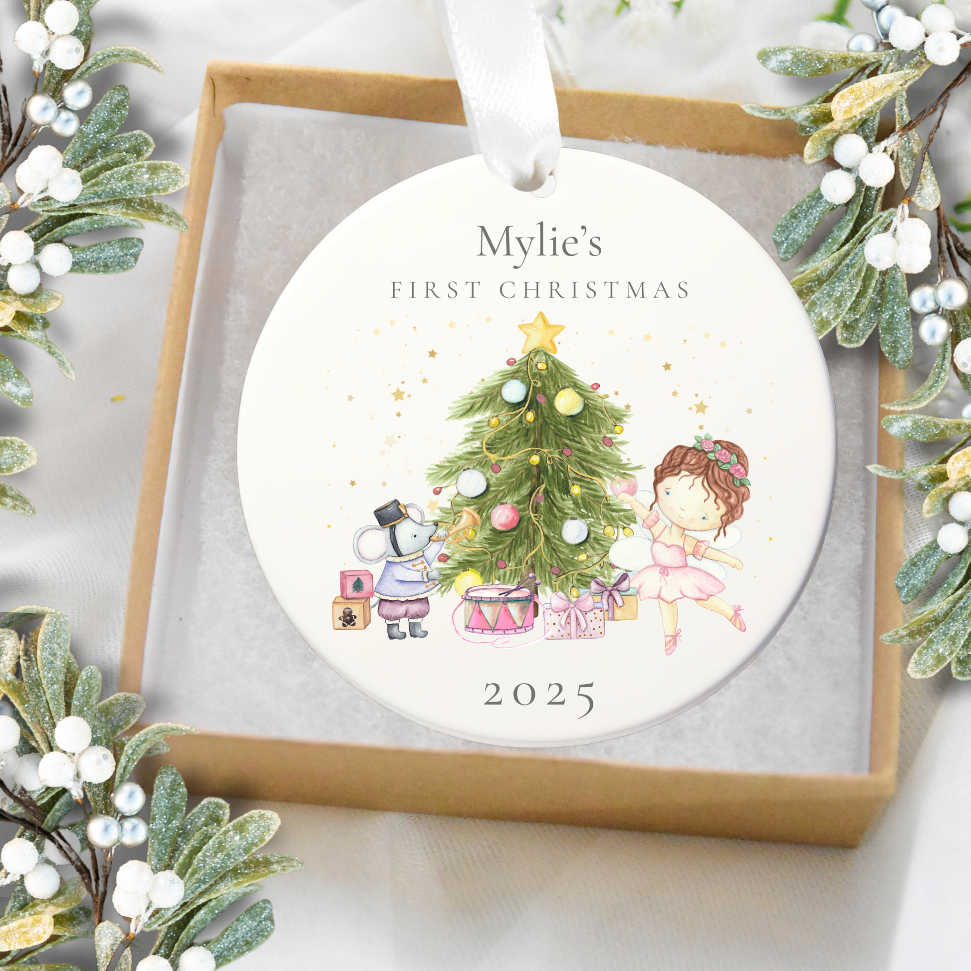Decorative ornament for 'Mylie's First Christmas 2025' with illustrations of a child, tree, and presents, surrounded by festive greenery.