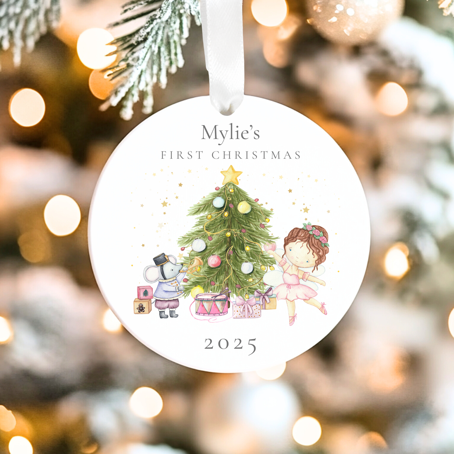 Decorative Christmas ornament with 'Mylie's First Christmas 2025' text and illustrations of a child and a mouse by a Christmas tree.