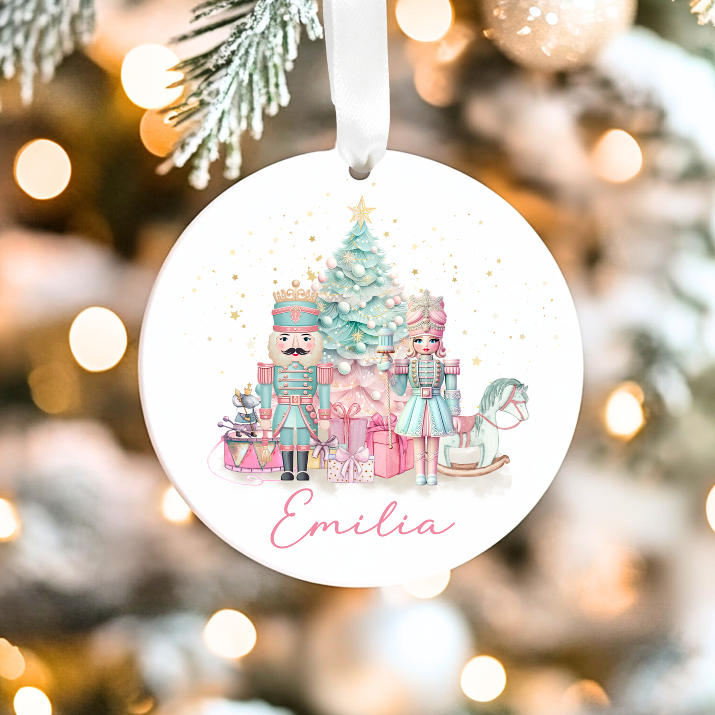 Christmas-themed ornament with Nutcracker design and 'Emilia' text, hanging against a blurred Christmas tree background.