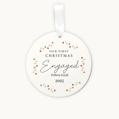 Round ceramic ornament with 'Our First Christmas Engaged' text and floral design on a white background