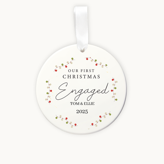 Round ceramic ornament with 'Our First Christmas Engaged' text and floral design on a white background