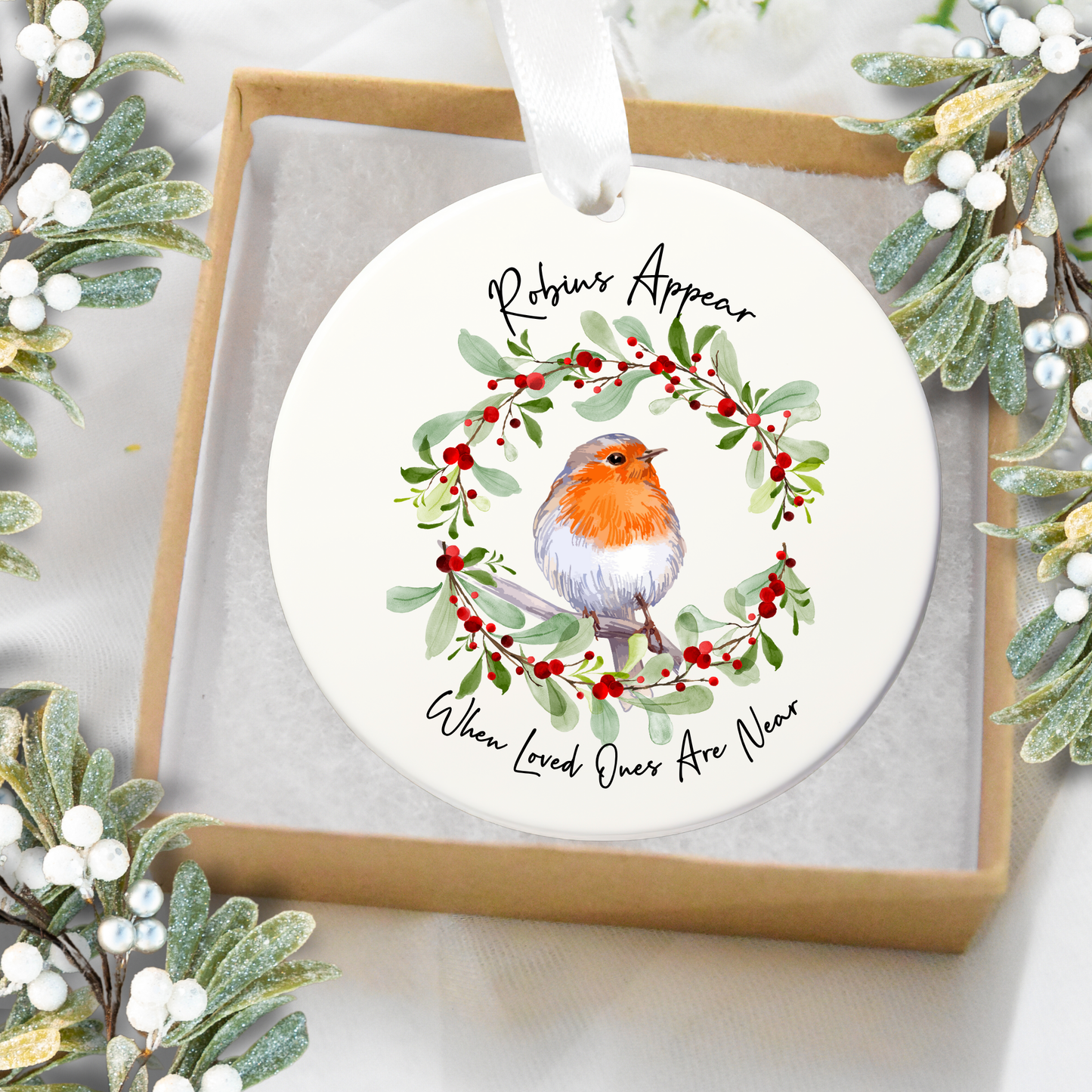 Round Christmas ornament with a robin and wreath design, surrounded by festive greenery.