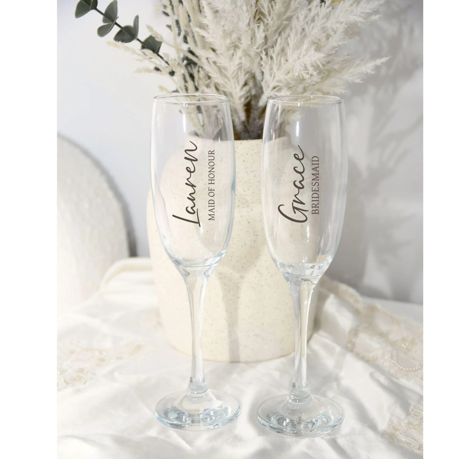 Two champagne flutes with personalized names on a white surface with decorative elements.