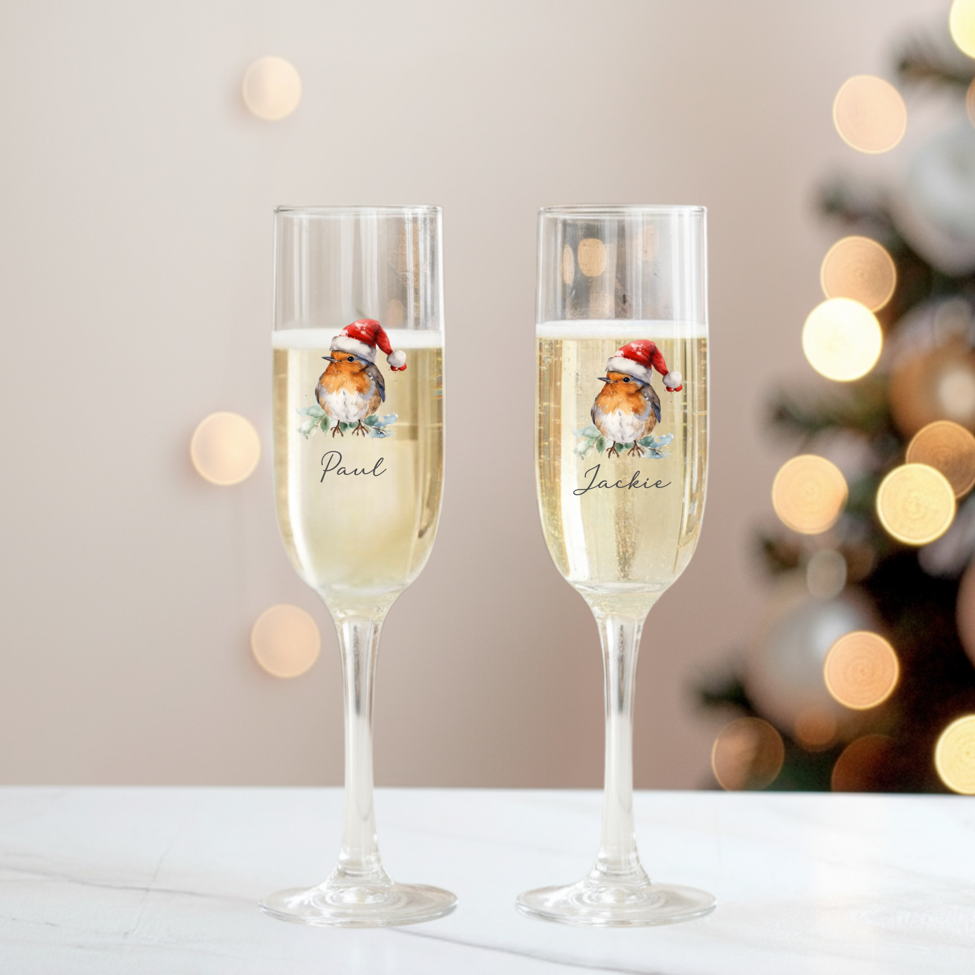 Two champagne flutes with Christmas-themed labels against a blurred festive background