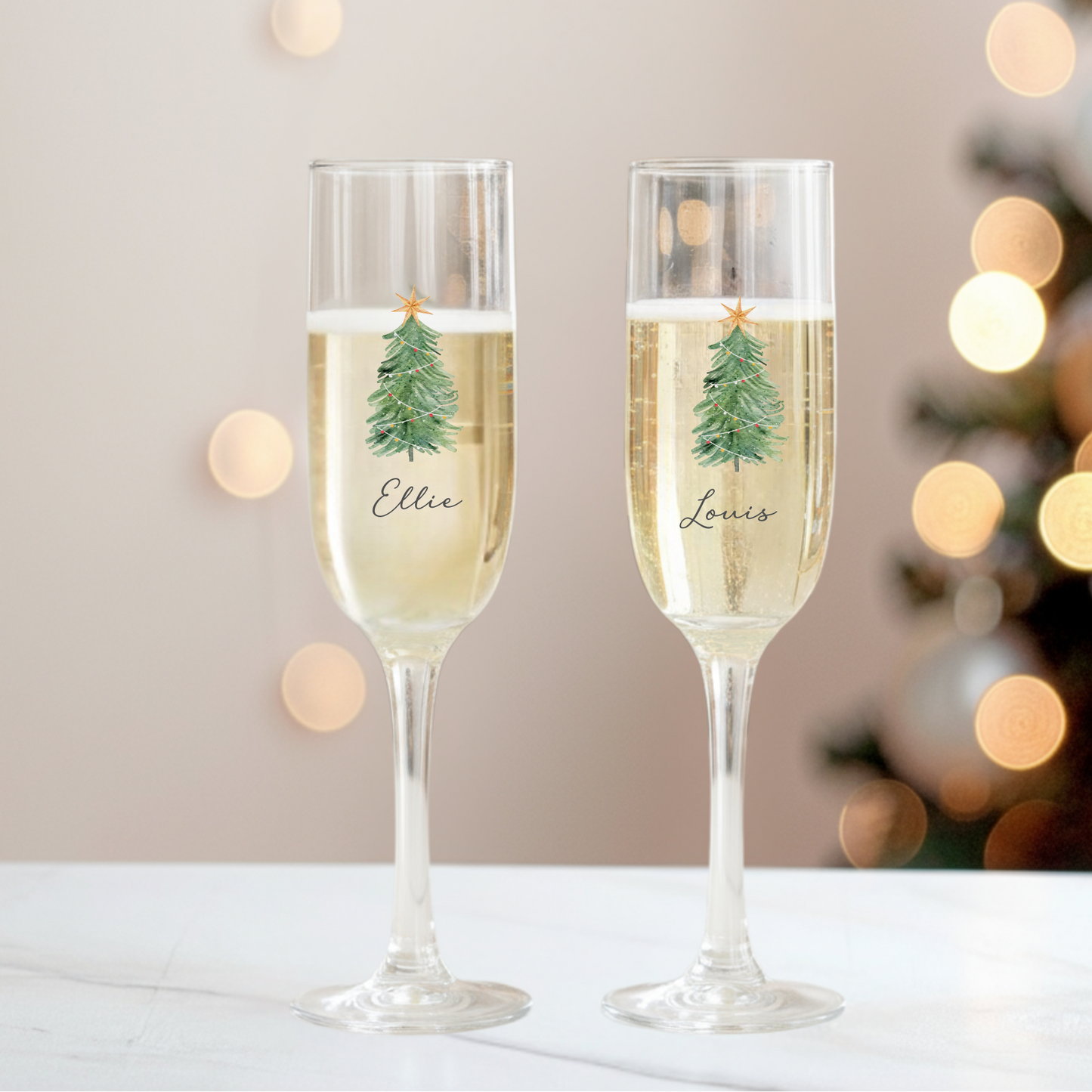 Two champagne flutes with Christmas tree designs and names 'Ellie' and 'Louise' against a festive background.