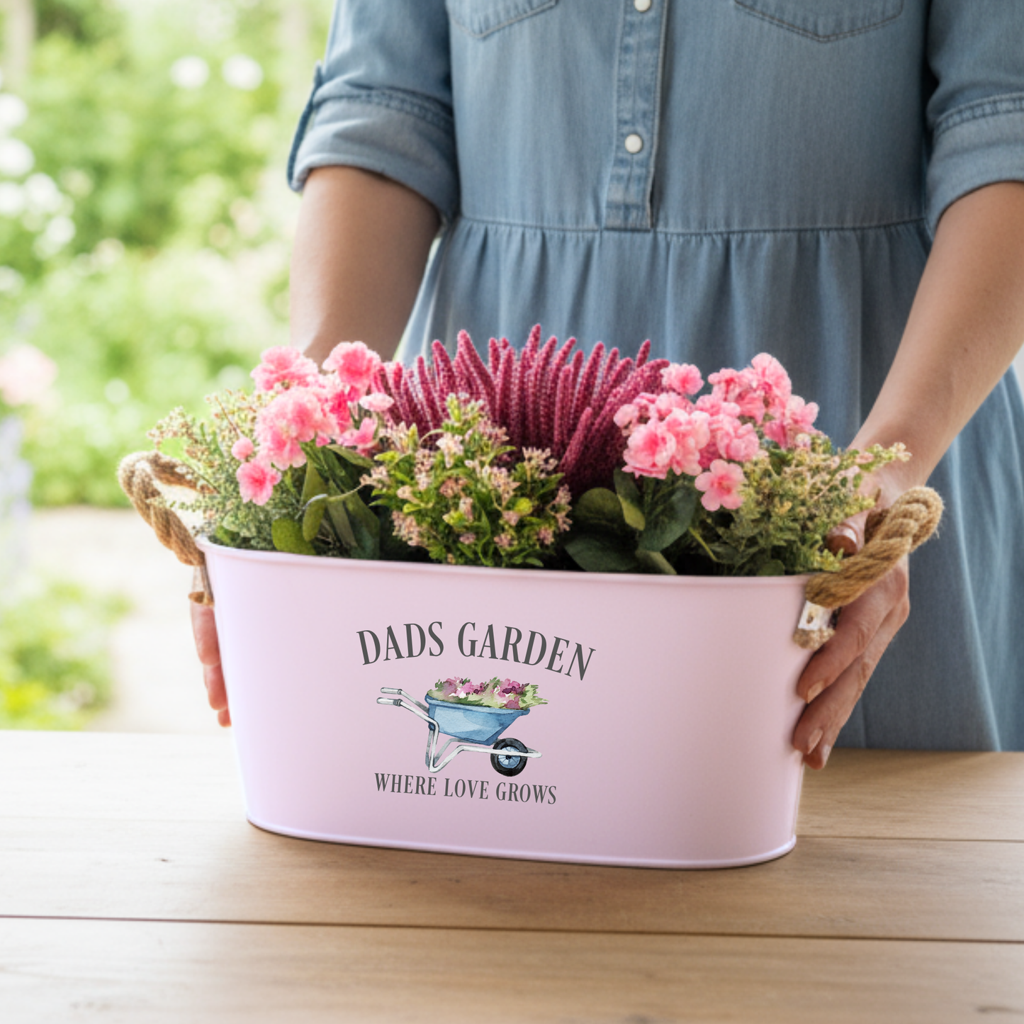 Person holding a pink planter with flowers and 'Dad's Garden' text.