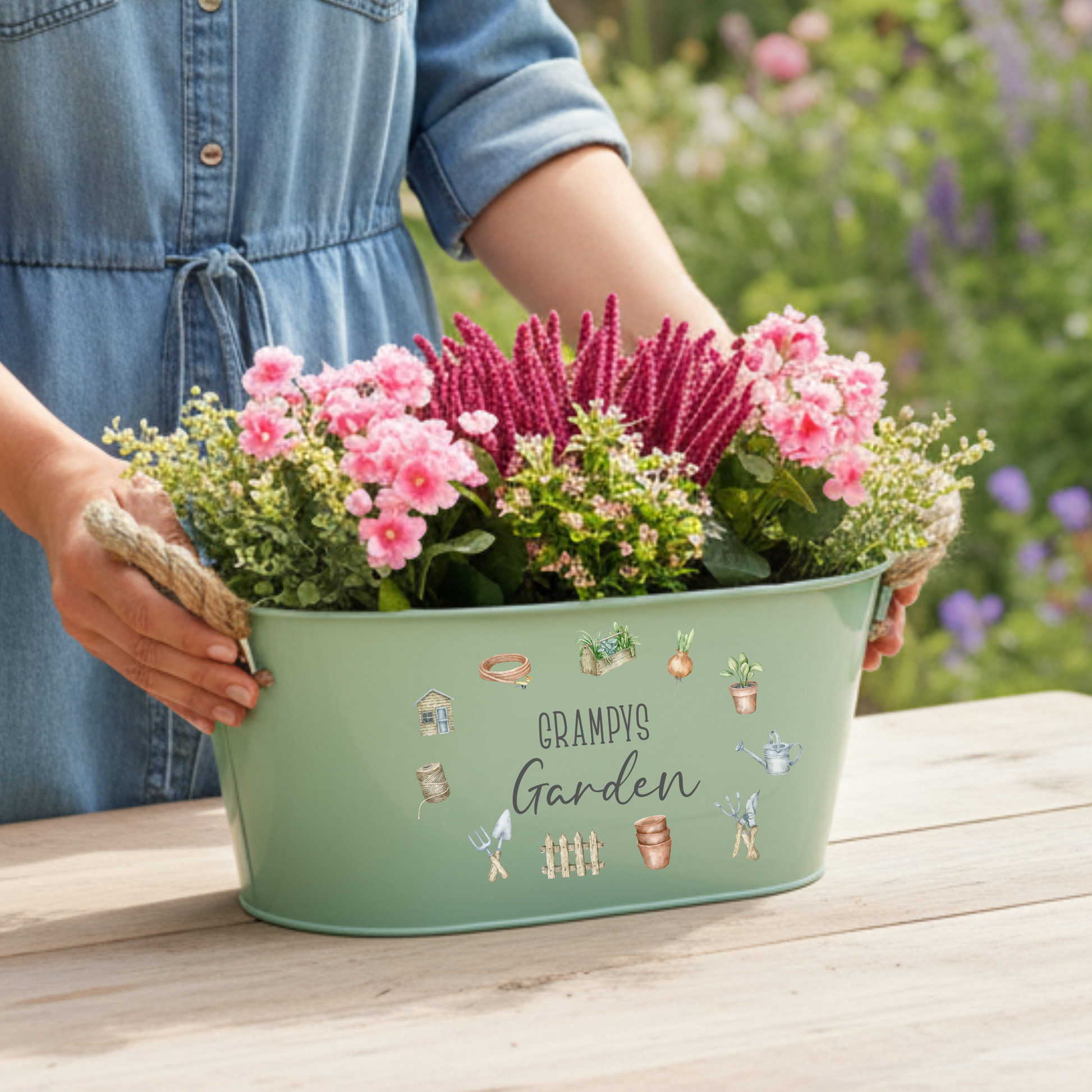 Person holding a green metal planter with flowers and 'Grampy's Garden' text.
