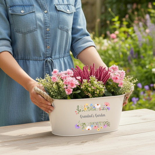 Person holding a planter with flowers labeled 'Grandad's Garden' in a garden setting.