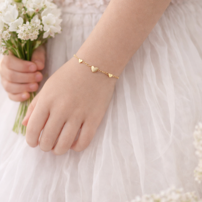 Child's hand wearing a gold heart-shaped bracelet holding a small bouquet of flowers.