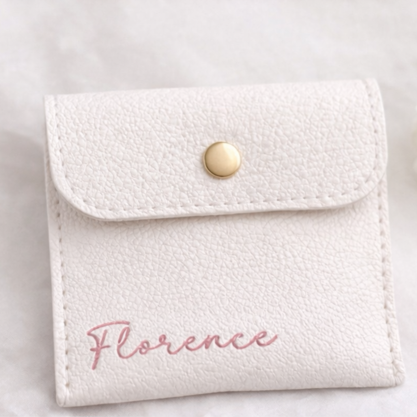 White textured pouch with 'Florence' and gold button on a light gray background