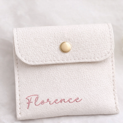 White textured pouch with 'Florence' and gold button on a light gray background