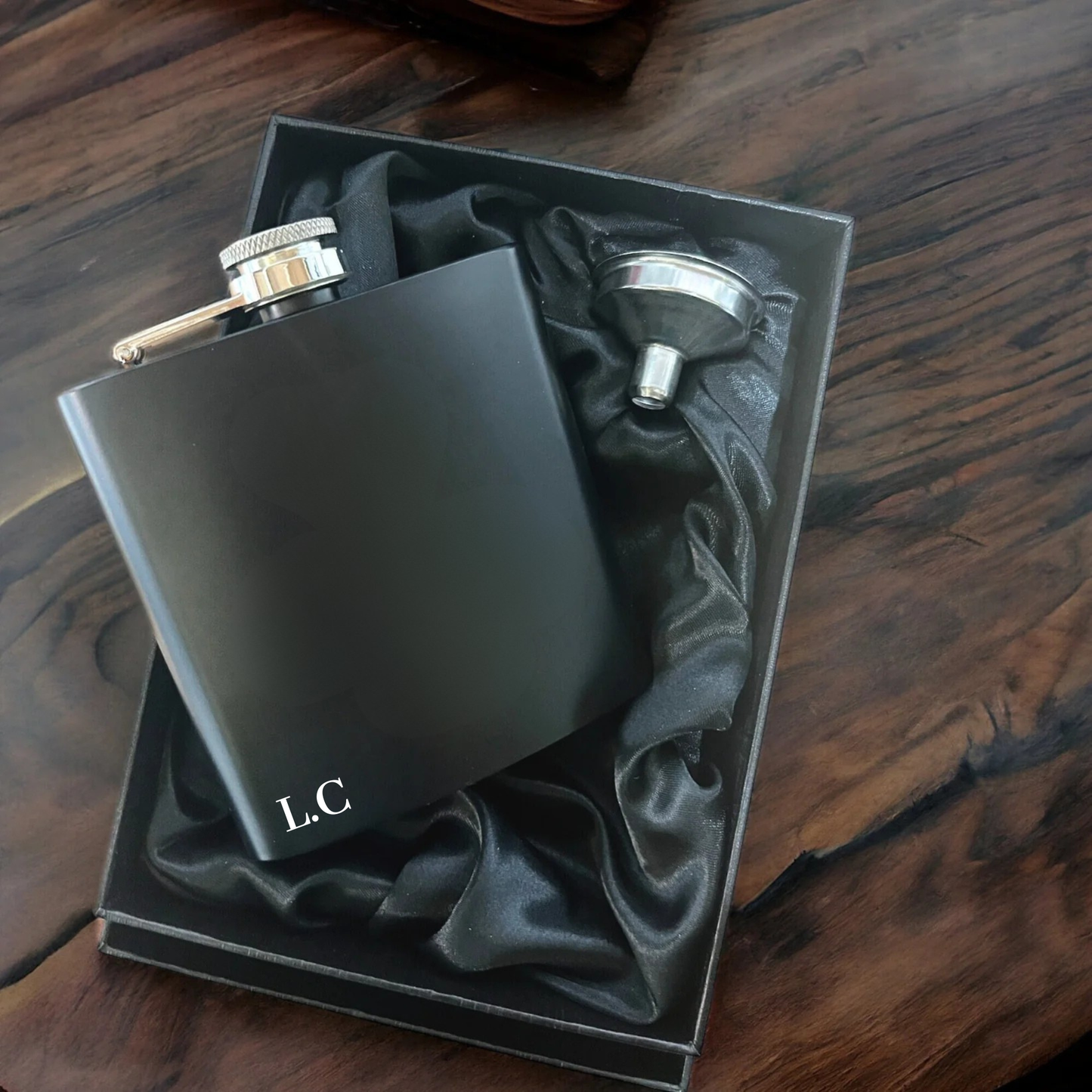 Black hip flask with gold cap and stopper in a black box on a wooden surface