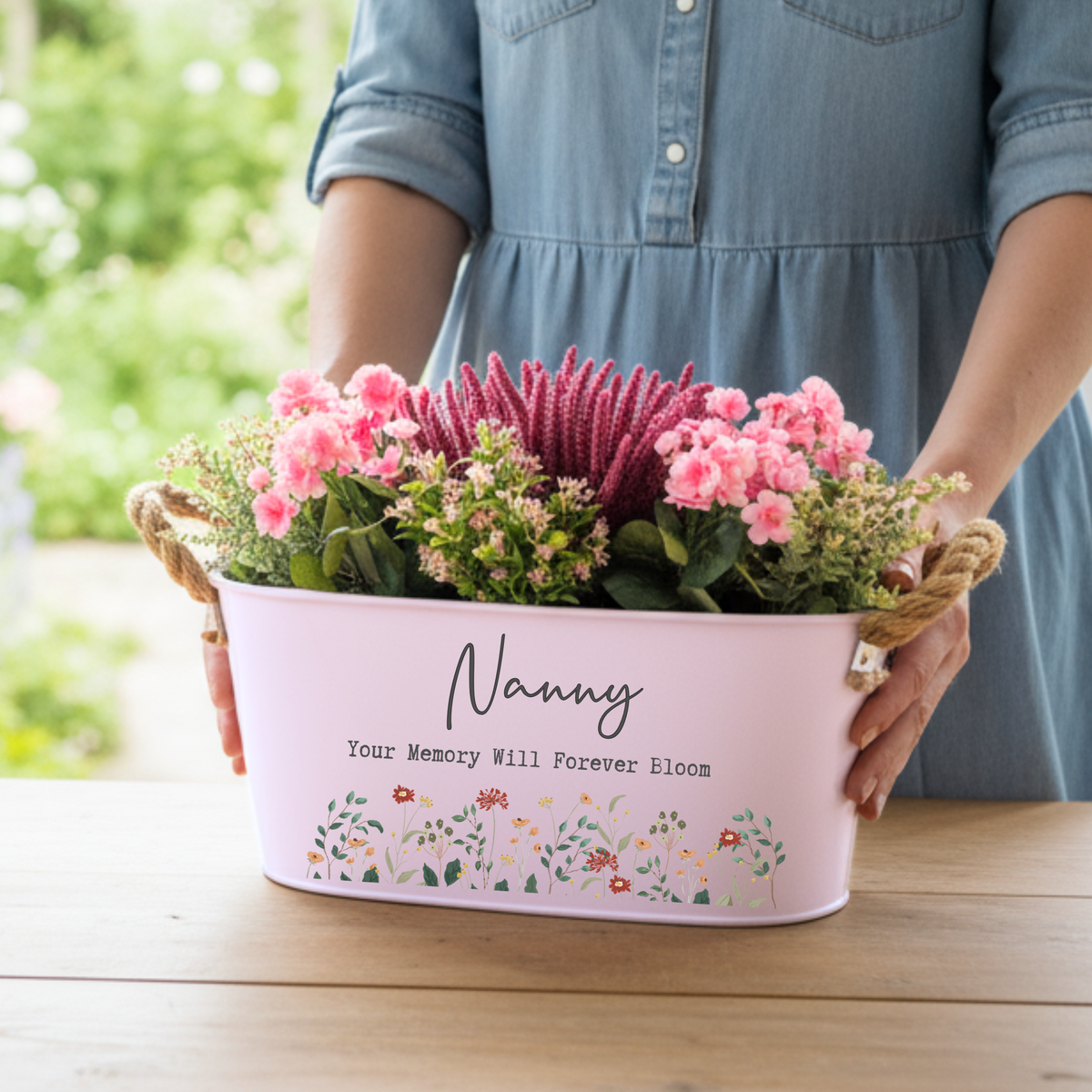 Person holding a pink floral arrangement in a decorative container with 'Nanny' text.
