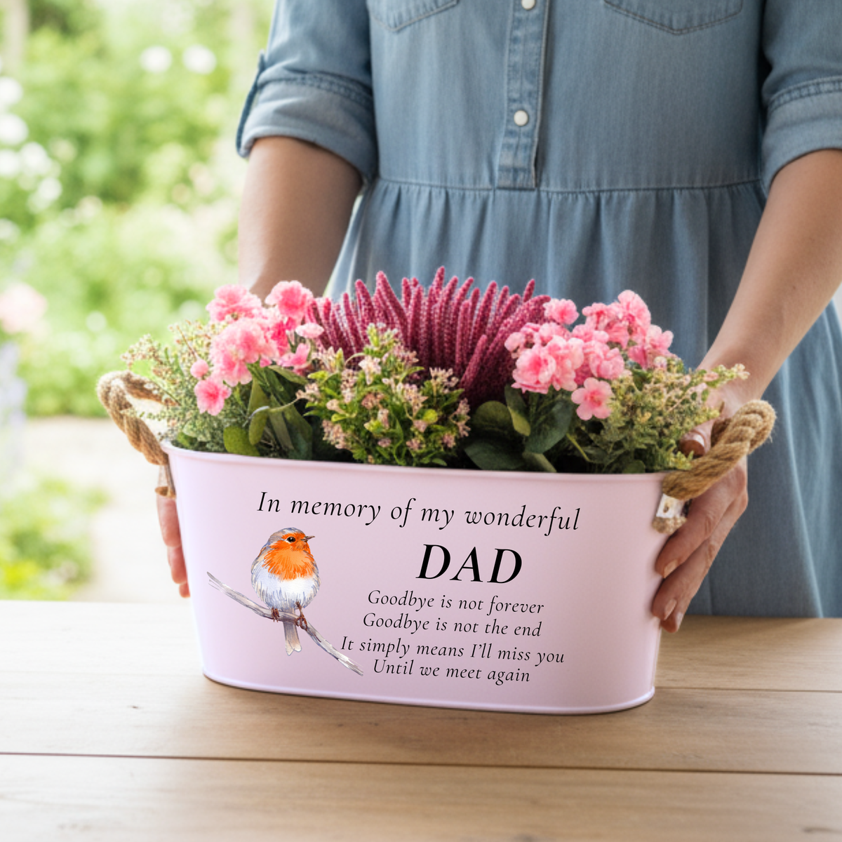 A woman holding Pink memorial planter printed with in memory of my wonderful Dadwith a robin illustration, with a garden background