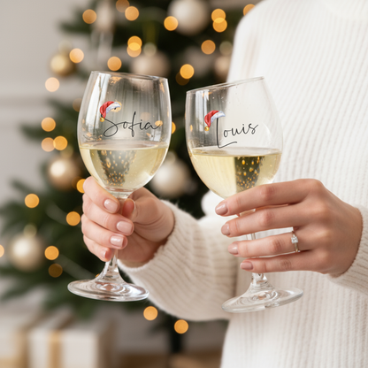 Two hands holding personalized wine glasses with a Christmas tree in the background