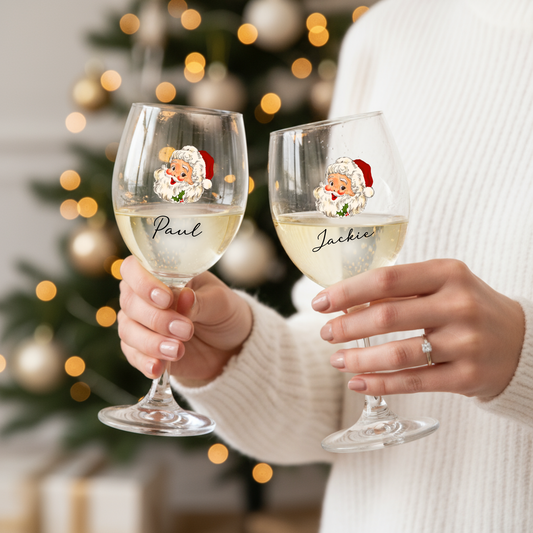 Two wine glasses with personalized names held by a person in front of a Christmas tree.