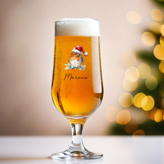 Beer glass with a festive design and 'Marcus' text, blurred Christmas tree in the background