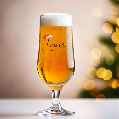 Glass of beer with 'Louis' and a Santa hat design, blurred Christmas tree in the background