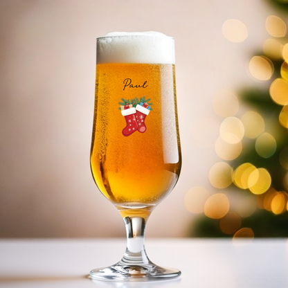 Glass of beer with a Christmas-themed design and 'Paul' text, blurred lights in the background