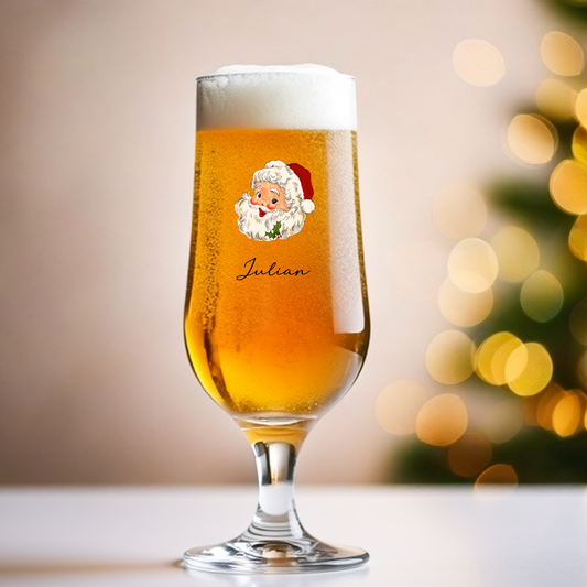 Glass of beer with a Santa Claus label and 'Julian' text, blurred Christmas tree in the background