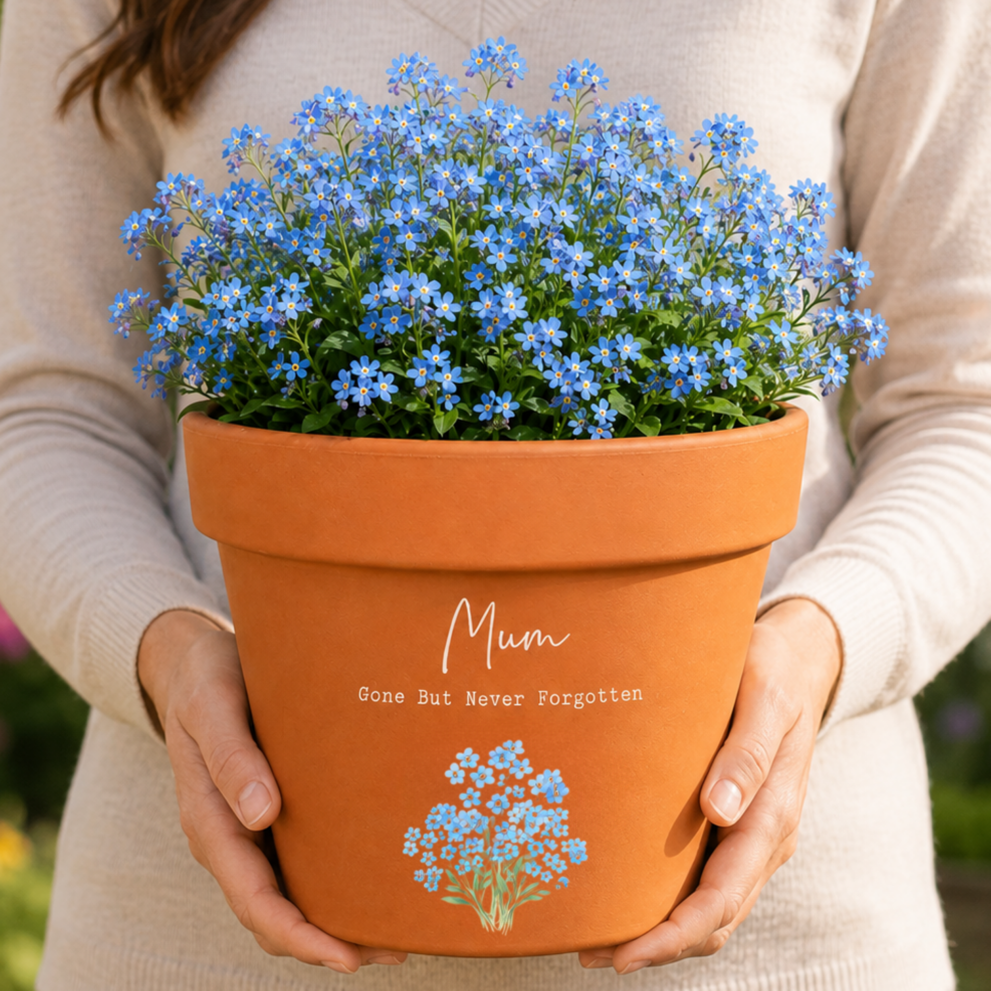 Person holding a potted plant with blue flowers and 'Mum Gone But Never Forgotten' text.