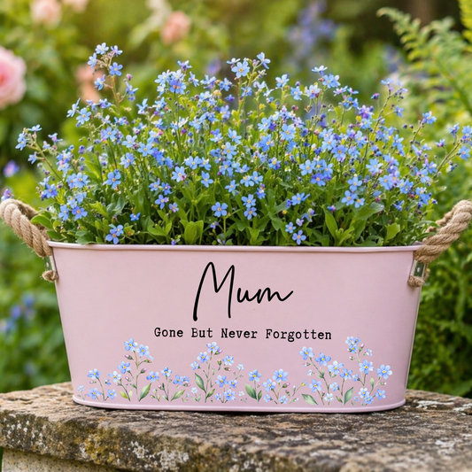 Pink metal planter with blue flowers and 'Mum Gone But Never Forgotten' text on a natural background