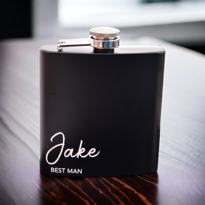 Black flask with 'Jake BEST MAN' engraving on a wooden surface