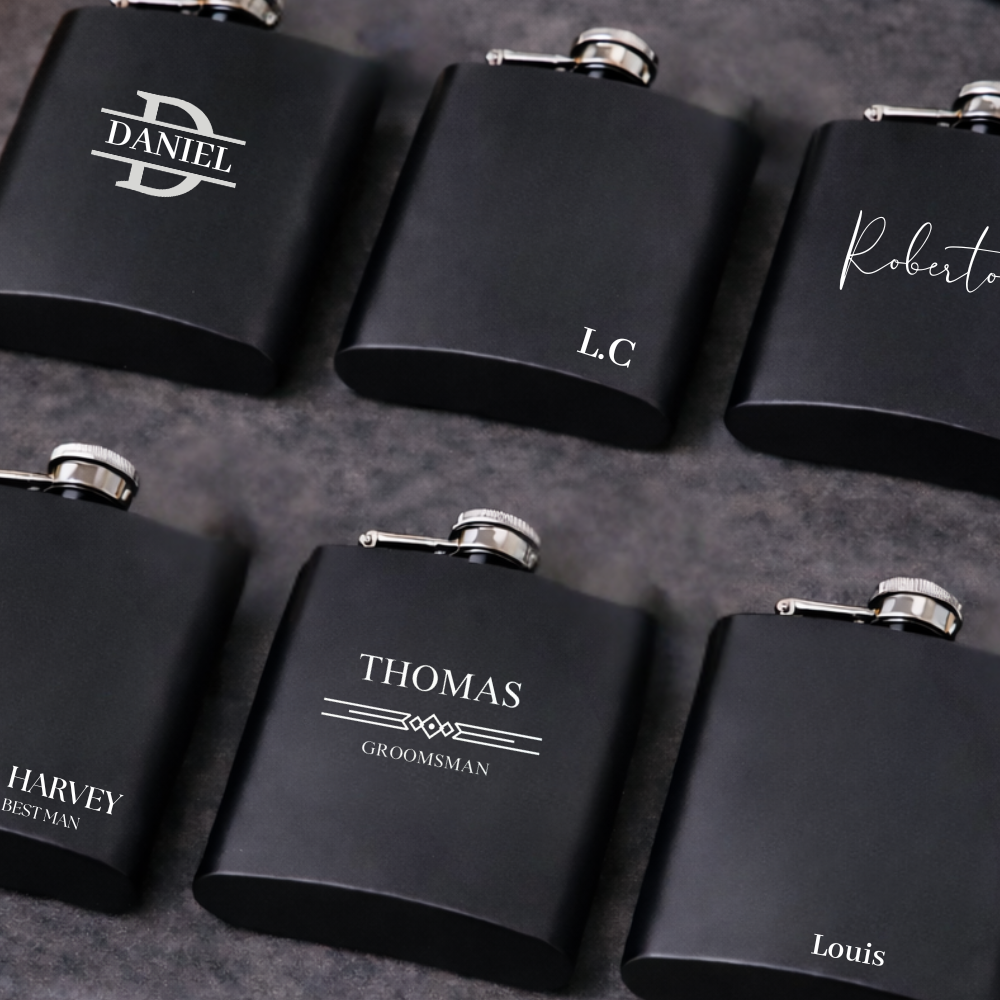 Set of wedding groomsman, best man, black flasks with personalised names on a dark surface