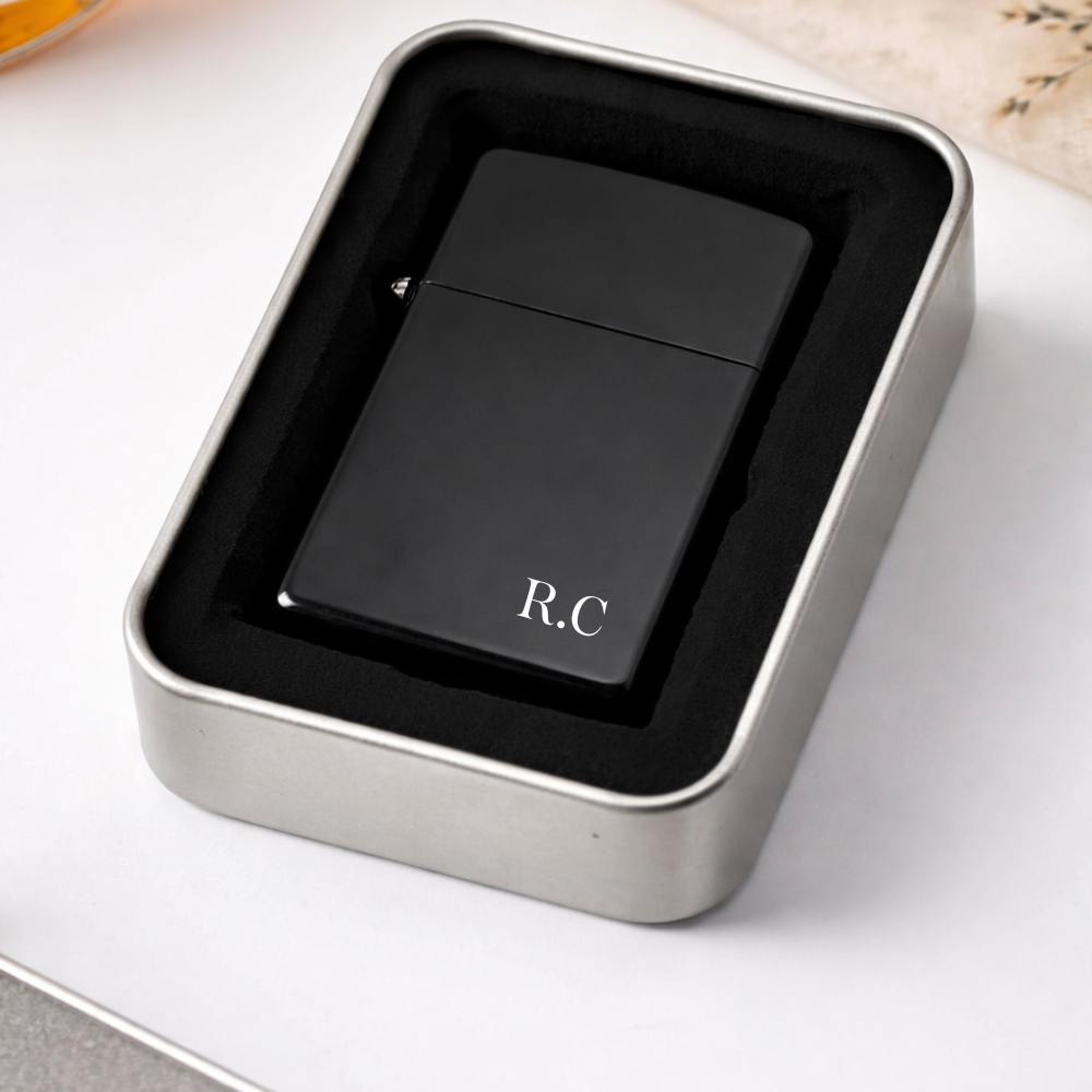 Black lighter with 'R.C.' initials in a metallic box on a white surface
