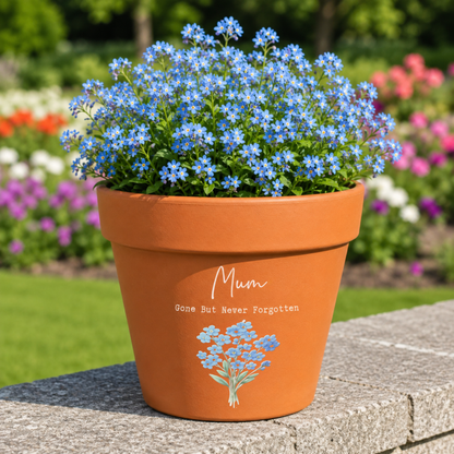 Terracotta pot with blue flowers and 'Mum Gone But Never Forgotten' text in a garden setting